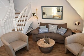 Una sala de estar con un sofá, dos sillones, una mesa de centro y una escalera.