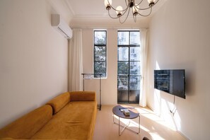 Una sala de estar con sofá, una mesita, televisor y ventana con cortinas.