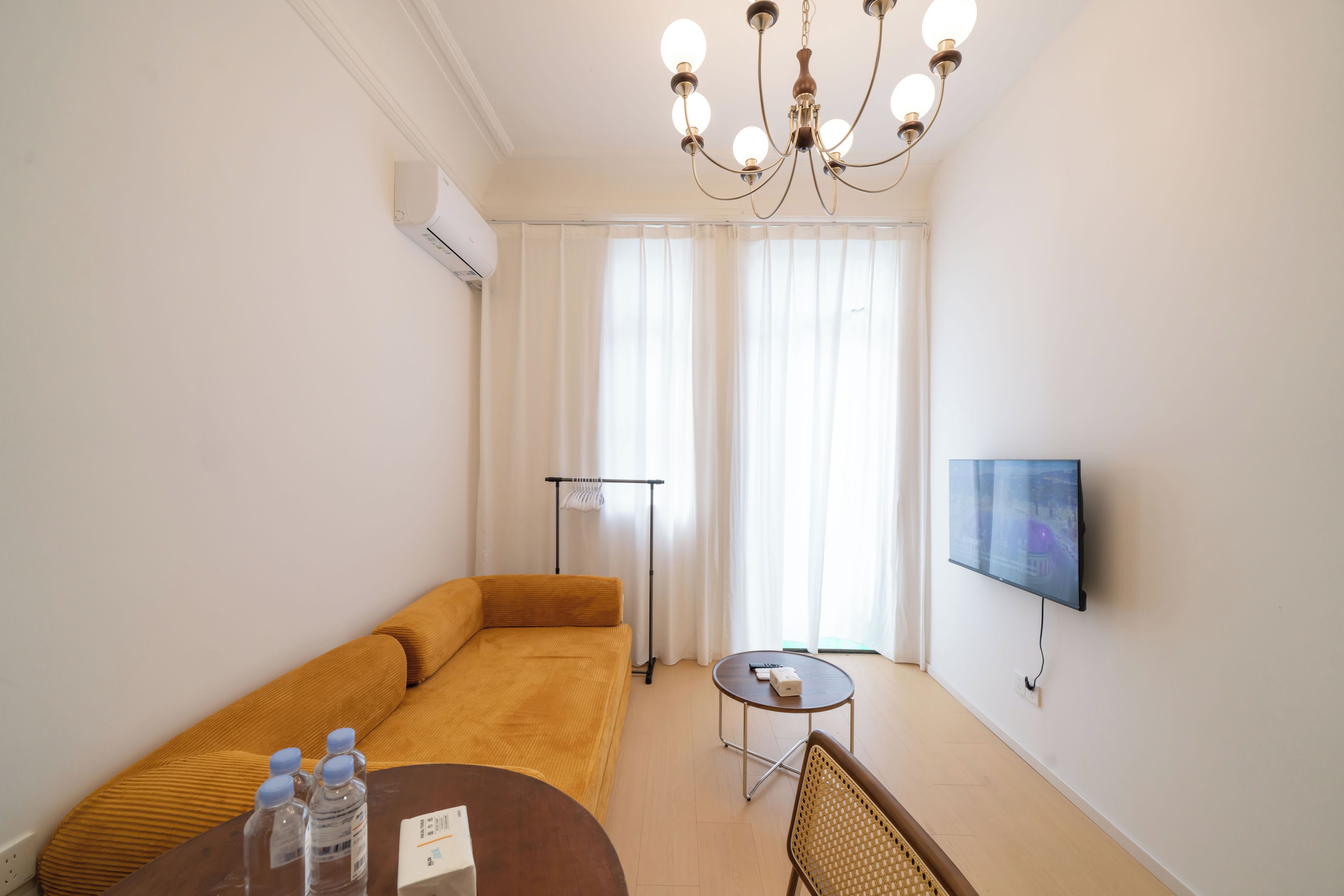 Ein modernes Wohnzimmer mit einer Couch, einem kleinen runden Tisch, einem an der Wand befestigten Fernseher und einer Deckenleuchte.