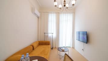 Ein modernes Wohnzimmer mit einer Couch, einem kleinen runden Tisch, einem an der Wand befestigten Fernseher und einer Deckenleuchte.