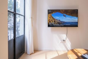 Una habitación con un ventanal grande, un televisor montado en la pared y una mesa de madera.