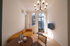 A modern living room with a sofa, a dining table with water bottles, a TV mounted on the wall, and a large window with curtains. - Book&Bed-People's Sq. Changzheng Hosp. (Shanghai)