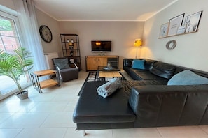 A living room with a black leather sofa, a wooden coffee table, a television, and a potted plant. - House with beach view (Varel\/Dangast)