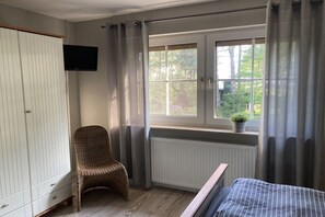 A bedroom with a bed, a wicker chair, a wardrobe, a television, a window with curtains, and a radiator. - House with beach view (Varel\/Dangast)