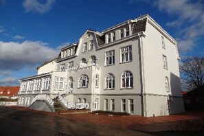 Ein großes, weißes, mehrgeschossiges Gebäude mit einer symmetrischen Fassade, zahlreichen Fenstern und einer zentralen Treppe.