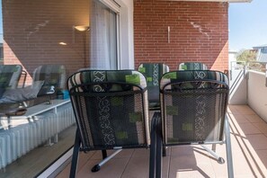 A balcony with two chairs and a table, a brick wall, and a window. - 10 at the new lighthouse (Borkum)