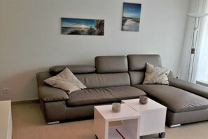 A modern living room with a sectional sofa, a small white side table, and two framed landscape paintings on the wall. - 10 at the new lighthouse (Borkum)