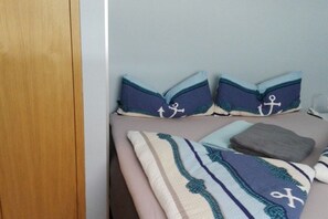 A bed with pillows and a blanket, a wooden door, and a light-colored wall. - 10 at the new lighthouse (Borkum)