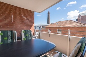 A balcony with a table and chairs, a brick wall, and a view of a tower. - 10 at the new lighthouse (Borkum)