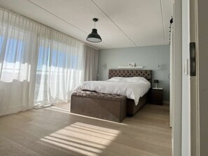 A bedroom with a large bed, a bedside table, a hanging light, and sheer curtains. - Holiday Home in Cadzand With Swimming Pool (Cadzand-Bad)