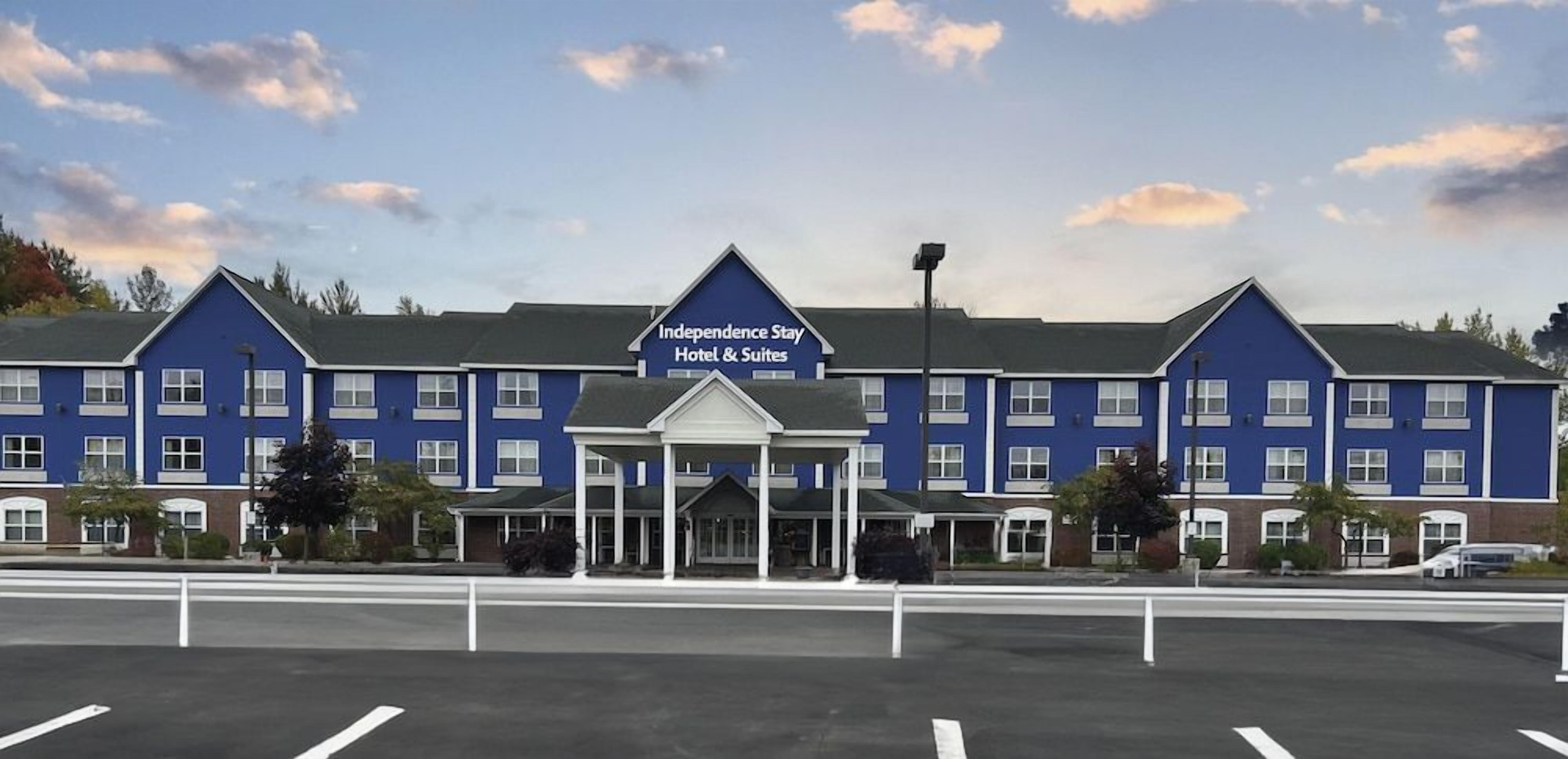 A hotel with a blue facade, a covered entrance, and a parking lot in front.