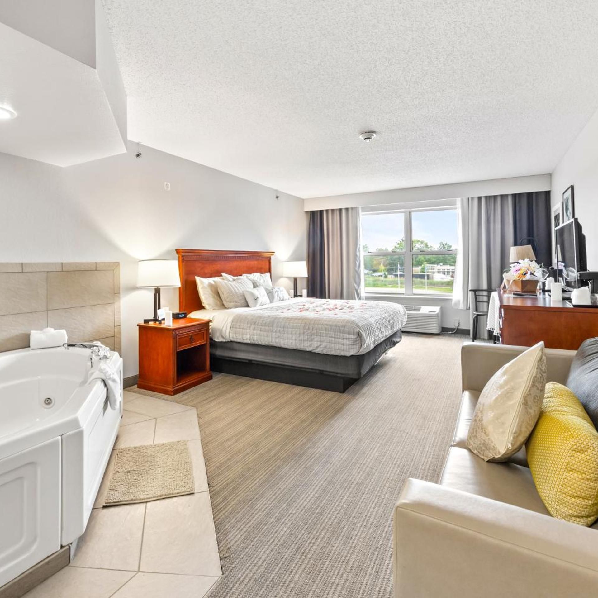 A hotel room with a large bed, a separate sofa, a desk, a TV, and a bathroom with a bathtub.