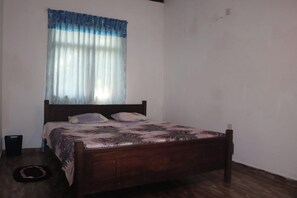 A bedroom with a wooden bed, a window with sheer curtains, and a plain white wall. - Vihansha Guesthouse Weligama  (Weligama)