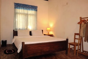 Un dormitorio con una cama de madera, una mesita de noche con lámpara, una ventana con cortinas y una silla de madera.