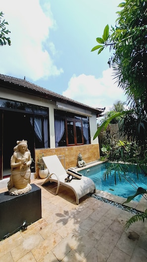 A poolside area with a lounge chair, a statue, and a building with a tiled roof.