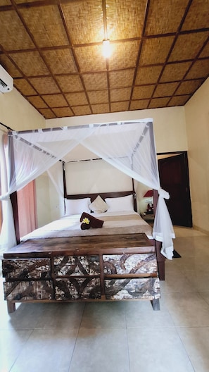 A bed with a canopy, a nightstand, and a wall-mounted air conditioning unit. - Gajah Biru Ubud (Ubud,Gianyar)