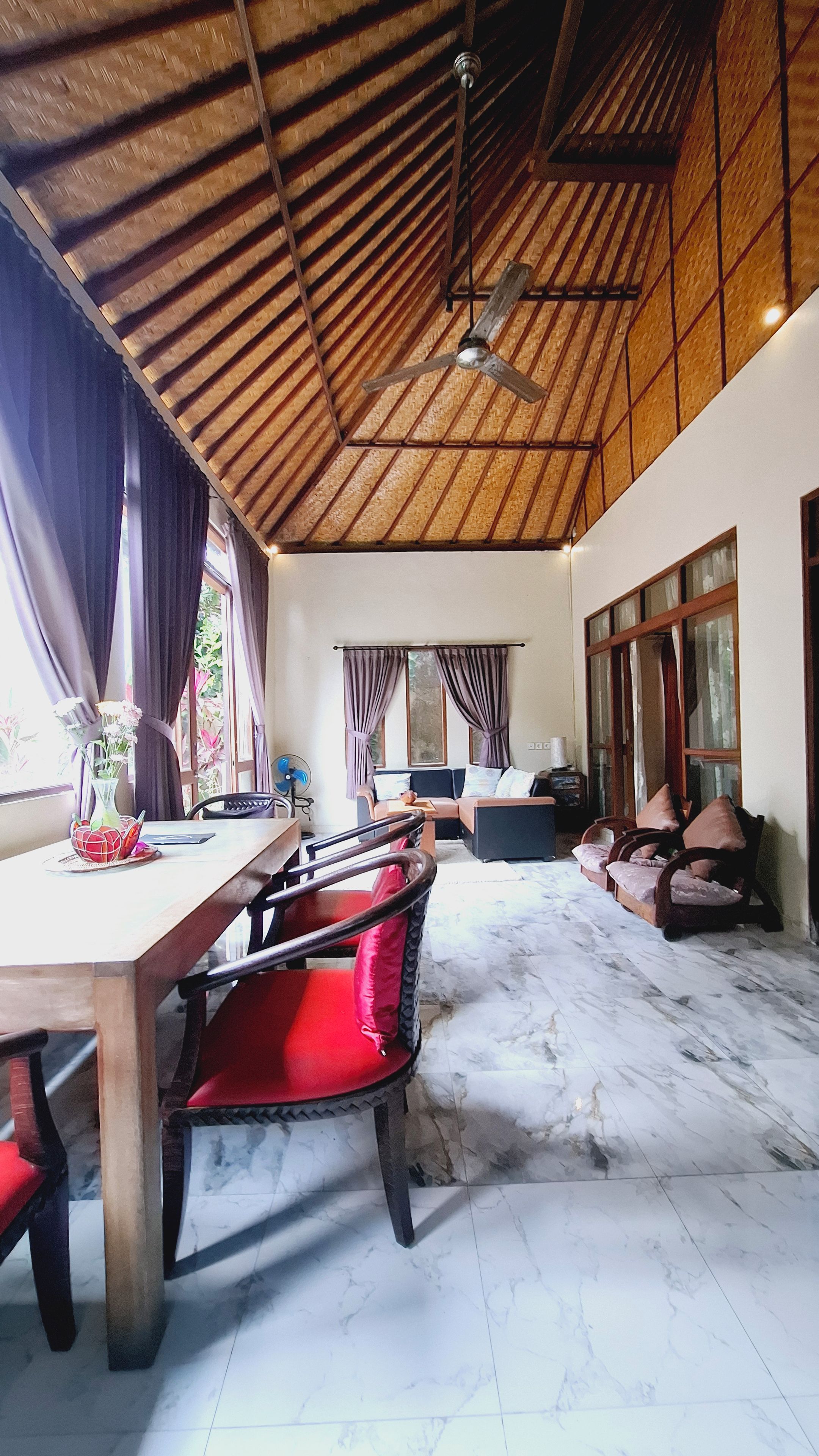 Una habitación amplia con techo alto, un comedor con mesa de madera y sillas rojas, y una sala de estar con sofás y televisor.