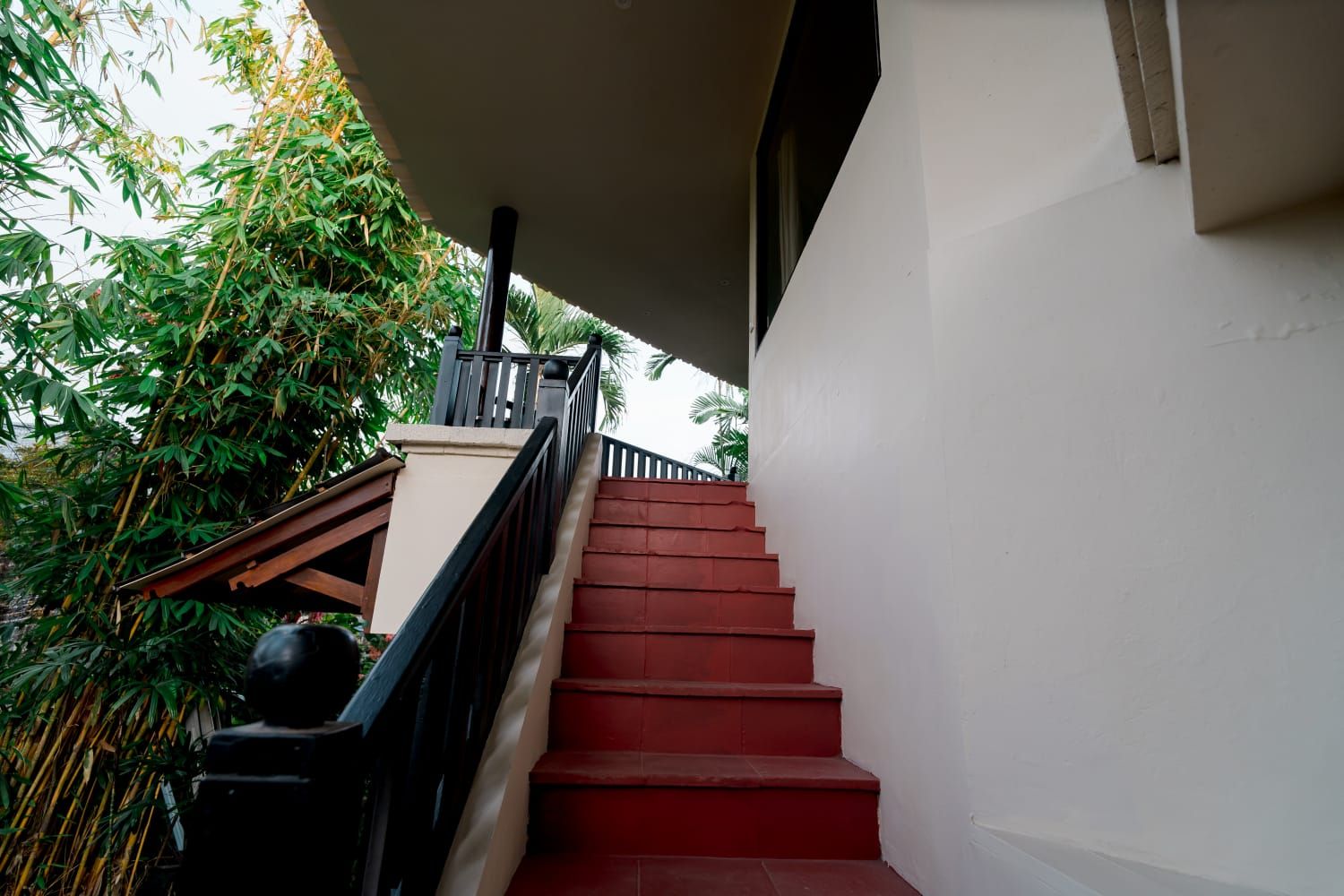 Una escalera con escalones rojos que sube a un balcón, rodeado de follaje.