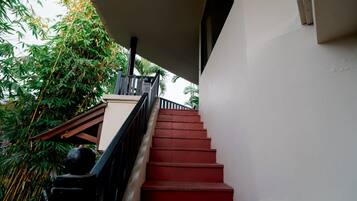 Una escalera con escalones rojos que sube a un balcón, rodeado de follaje.