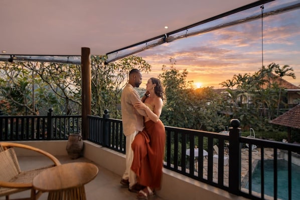 A couple embracing on a balcony with a view of a sunset and tropical vegetation. - Gajah Biru Ubud (Ubud,Gianyar)