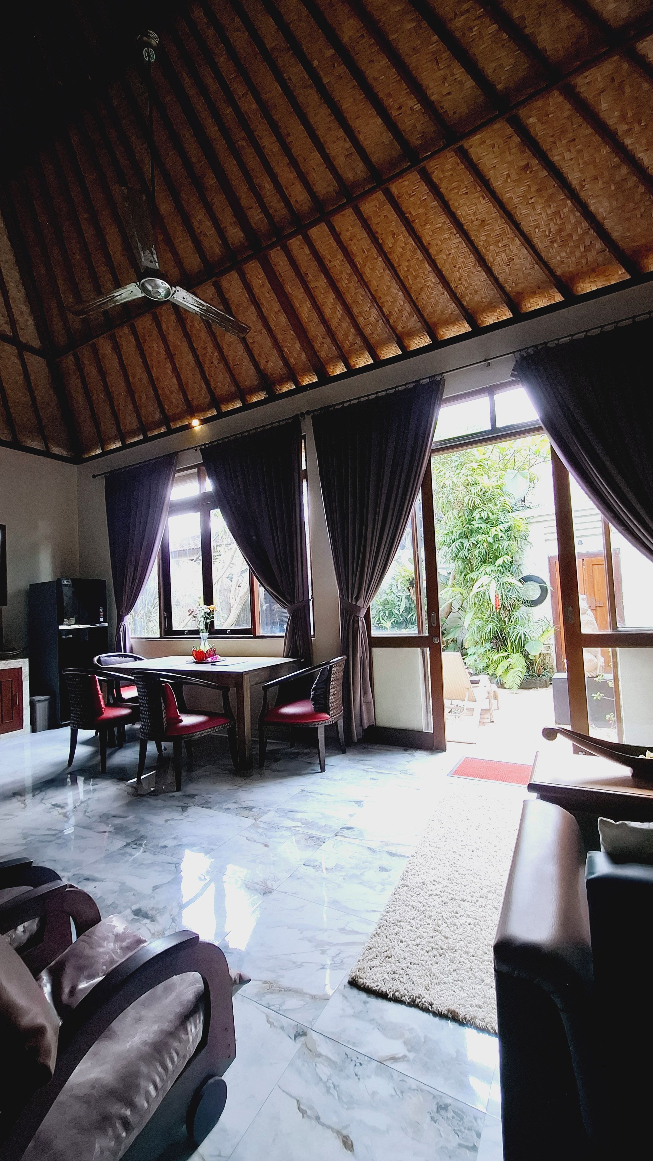 Una habitación amplia con techo alto, un comedor con sillas y mesa, y ventanas grandes con cortinas.