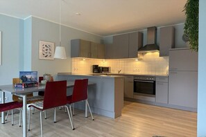 A modern kitchen with grey cabinets, a central island, and a dining area with red chairs. - South Beach Loft Borkum (Borkum)