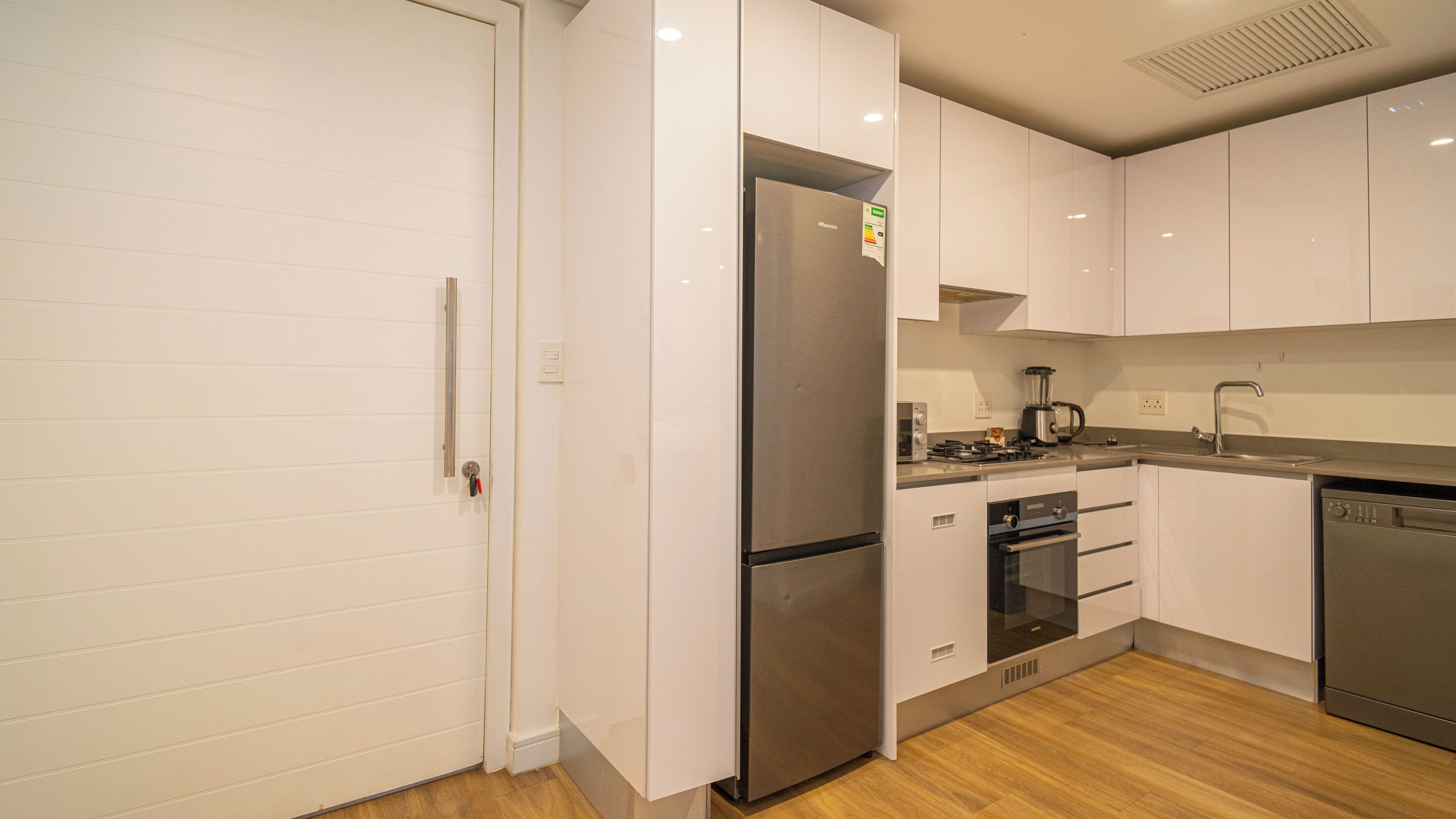 A modern kitchen with white cabinetry, stainless steel appliances, and a wooden floor.
