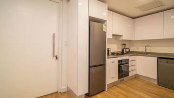 A modern kitchen with white cabinetry, stainless steel appliances, and a wooden floor.