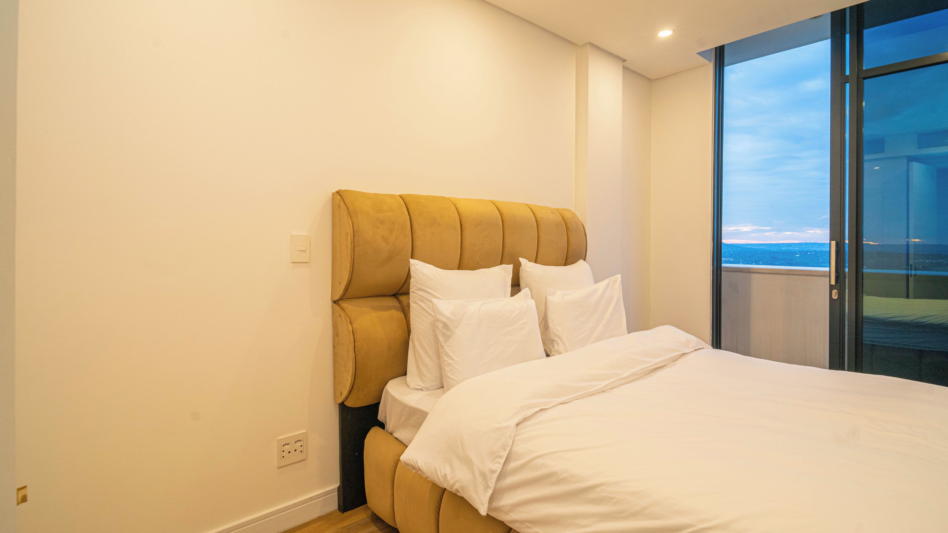 Une chambre à coucher avec un grand lit, une tête de lit et une vue sur l’extérieur, visible à travers une porte vitrée.