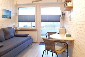 Um espaço compacto com sofá, mesa de jantar, cadeiras de vime e vista através de uma porta.