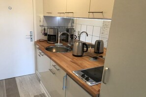 Cozinha compacta com pia de aço inoxidável, cafeteira, chaleira e torradeira.