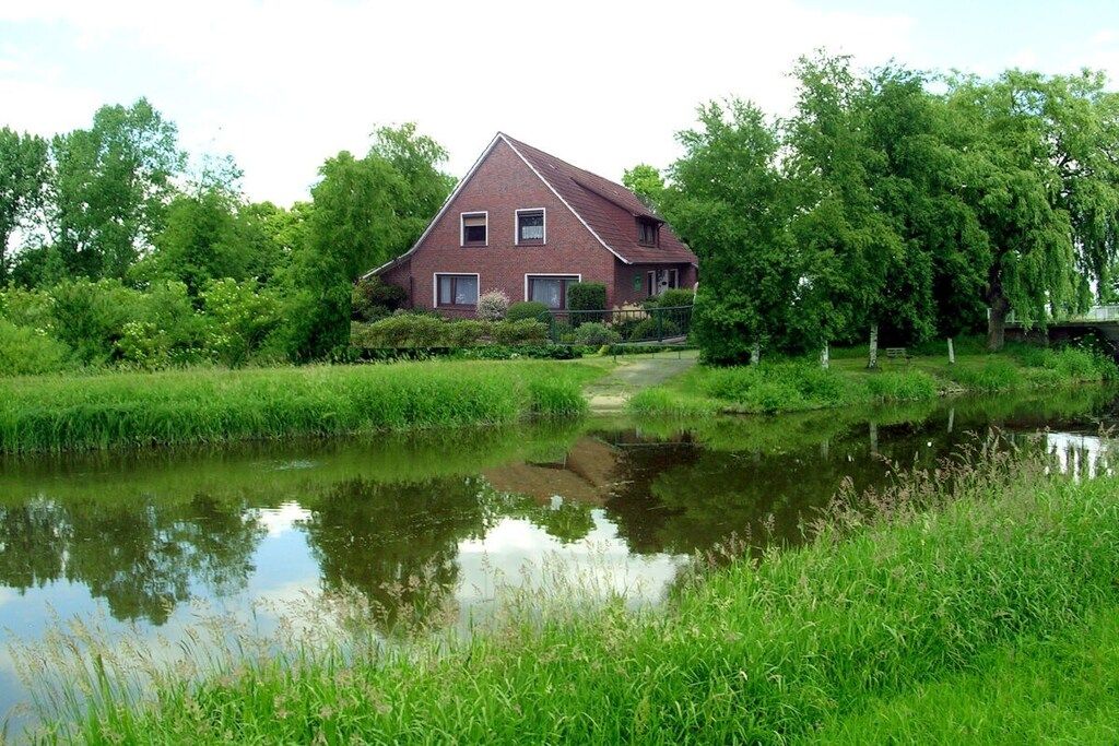 Ein einstöckiges Backsteinhäuschen mit geneigtem Dach, umgeben von üppiger Vegetation und einem kleinen Teich.