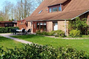 A two-story brick house with a sloped roof, a patio with outdoor furniture, and a well-maintained garden. - Holiday home in Detern with swimming pool (Detern)
