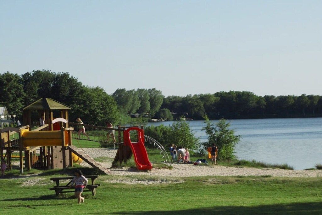 Un parc au bord du lac, équipé d’aires de jeux, de tables de pique-nique et d’une structure en bois.