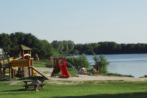 A lakeside park with playground equipment, picnic tables, and a wooden structure. - Holiday home in Detern with swimming pool (Detern)