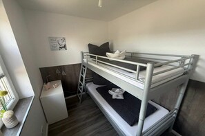 A bunk bed room with a ladder, a small white desk, and a window with a plant. - Bungalow with 1 bedroom (Dornum - Dornumersiel)