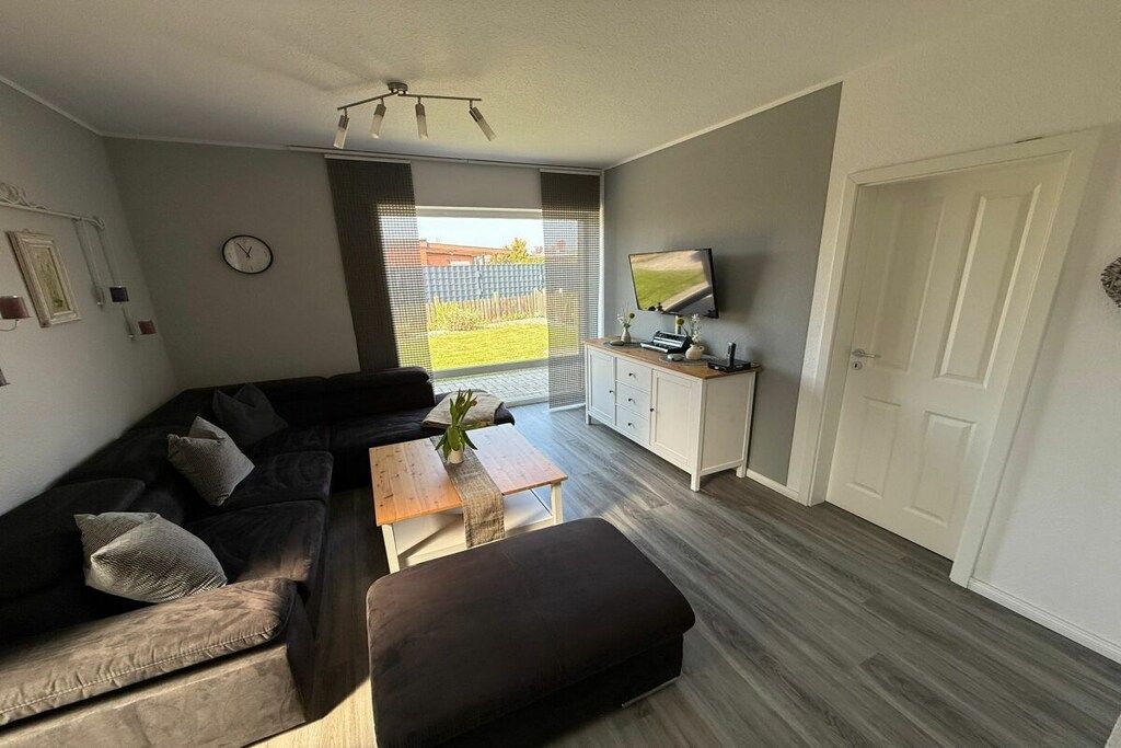 Een moderne woonkamer met een hoekbank, een salontafel, een tv op een kast en een deur aan de rechterkant.