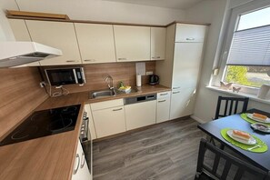 A compact kitchen with a microwave, stove, sink, and a dining area with a table and chairs. - Bungalow with 1 bedroom (Dornum - Dornumersiel)