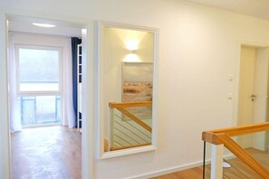 A hallway with a wooden staircase, a mirror with a light, and a door leading to another room. - Holiday home in Lancken with swimming pool (Lancken)