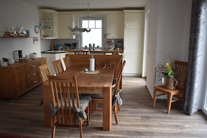 A dining area with a wooden table and chairs, a kitchen in the background, and a window providing natural light. - Holiday home in Breege with swimming pool (Breege)