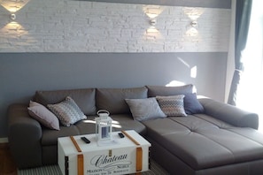 A modern living room with a grey sofa, a white coffee table with a bottle, and a brick wall with wall sconces. - Holiday apartment in Binz with swimming pool (Binz)