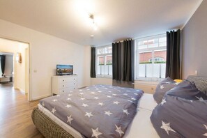 Ein Schlafzimmer mit Bett, Fernseher, Kommode und einem Fenster mit Vorhängen.