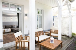 An outdoor seating area with wooden furniture and a table, a white wall, and a window. - Holiday apartment in Binz with swimming pool (Binz)