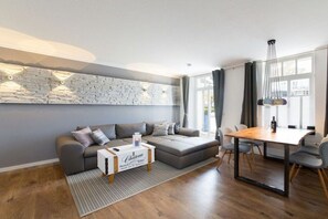 Ein modernes Wohnzimmer mit einem grauen Ecksofa, einem Holztisch und einem Esstisch mit Stühlen.