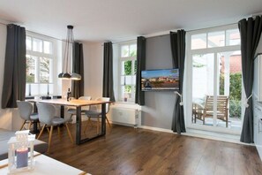 Ein modernes Zimmer mit Essbereich, einem an der Wand befestigten Fernseher und großen, mit Vorhängen versehenen Fenstern.