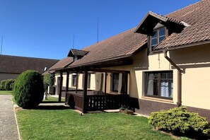 A two-story building with a covered patio area, a well-maintained lawn, and a large bush. - Valahof fattening barn (Milevsko)