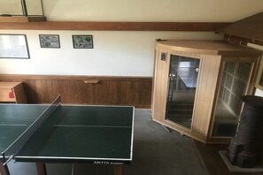 Une table de ping-pong avec un banc en bois, une armoire en bois dotée de portes en verre et une cheminée.