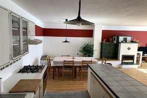 A kitchen with a dining table, chairs, a stove, cabinets, and a fireplace. - Valahof fattening barn (Milevsko)