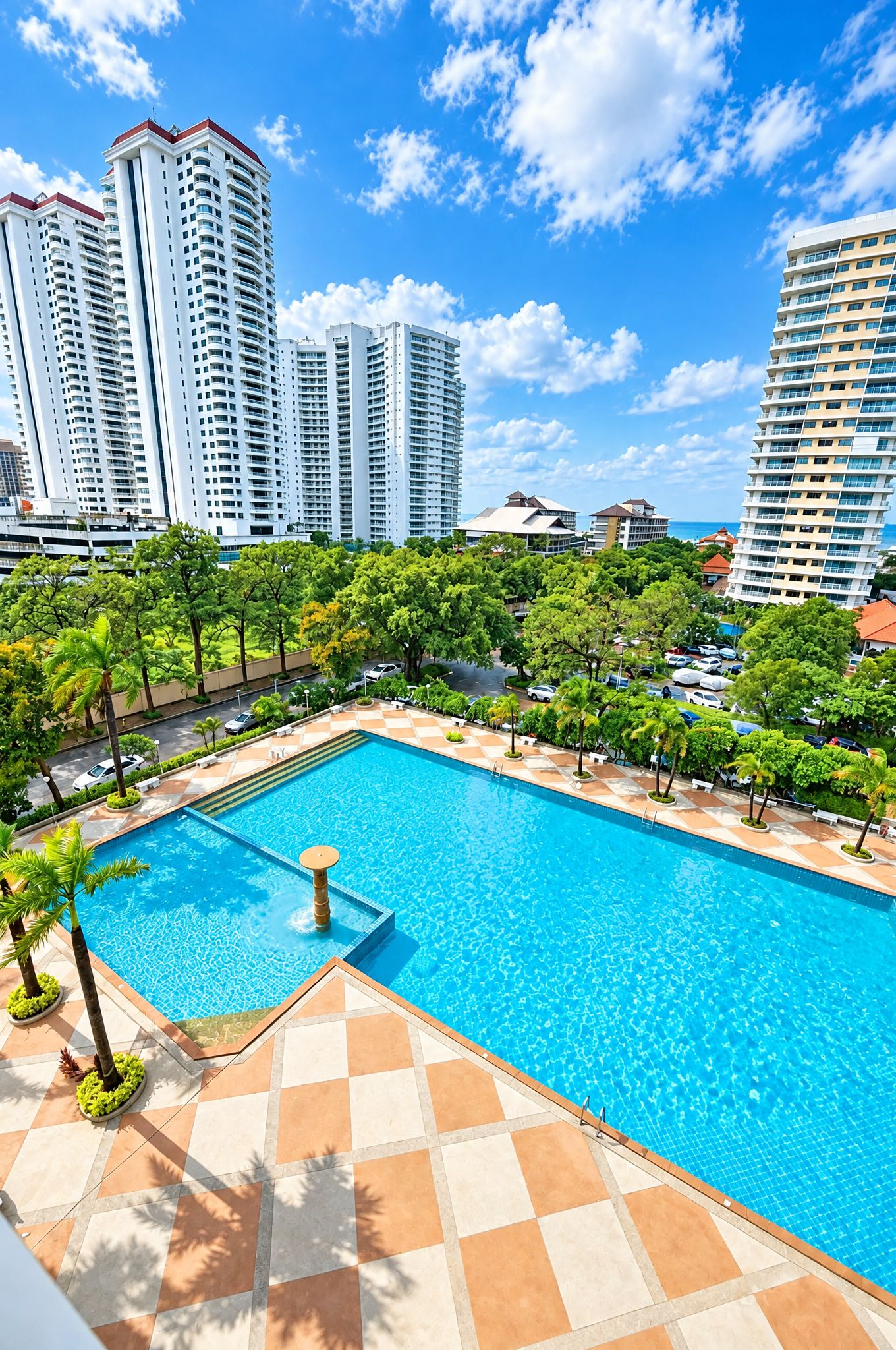 A swimming pool with a tiled deck, surrounded by palm trees and buildings in the background.