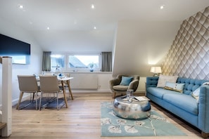A modern living room with a dining area, a blue sofa, and a patterned rug. - Holiday apartment in List with swimming pool (List)